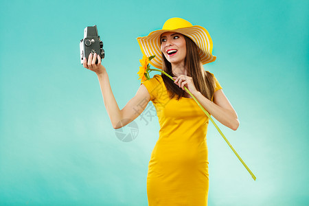 夏天的女人穿着连衣裙帽子,戴着向日葵,用老式相机生动的蓝色背景上拍照图片