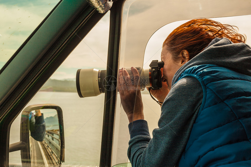 成熟的女旅游专业摄影师用相机露营车上拍照,开车上路女乘客窗外拍照,刮风的天气摄影师露营车里拍照图片