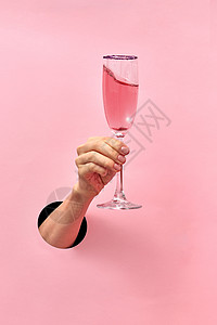女人的手洞里着璃与玫瑰酒个柔的粉红色背景,假日玫瑰酒杯女的手墙上的洞图片