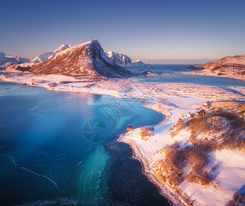 冰峡湾日落时,雪覆盖着山脉房屋清澈的水蓝天冬季景观与海岸,雪岩,罗布,道路挪威洛福滕群岛小村庄的顶部景观背景