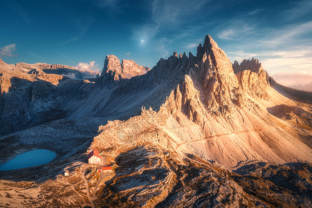 秋天日落时,山上美丽的房子教堂风景与建筑物,高岩石,湖泊蓝天与月亮云黄昏意大利白云石TreCime公园的鸟瞰图背景图片