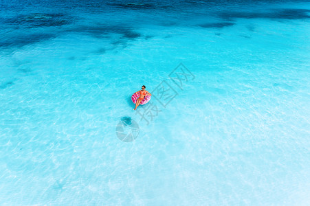 海中游泳女孩位轻女子夏天日落时用粉红色的甜甜圈游泳圈清澈的蓝色大海中游泳的鸟瞰图热带航空景观与女孩,清澈的蔚蓝水,沙滩的背景
