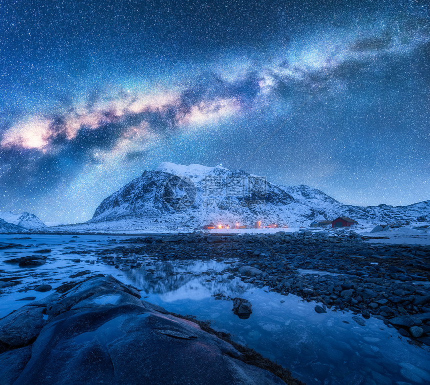 雪上的银河覆盖了冬天的山脉岩石海滩挪威洛福腾群岛着蓝色星空水石头雪岩明亮的星系城市灯光的景观图片