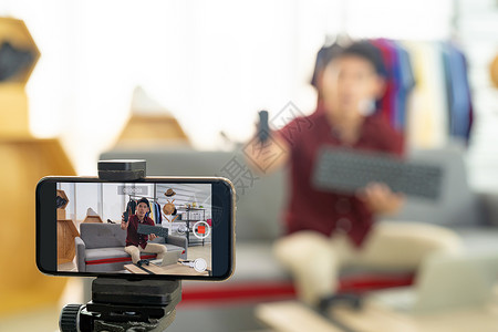 轻的亚洲男线商家博主用智能手机录制场景Vlog视频,以查看IT产品线Influencer关于社交媒体专注于背景图片