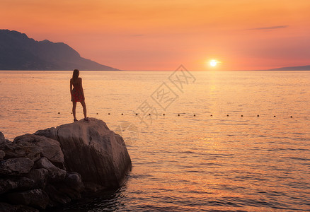日落站在海边岩石上的女人图片