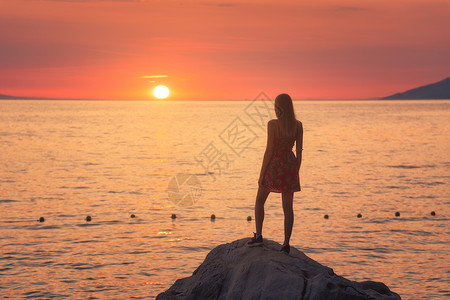 女人日落时站在海边的岩石上图片