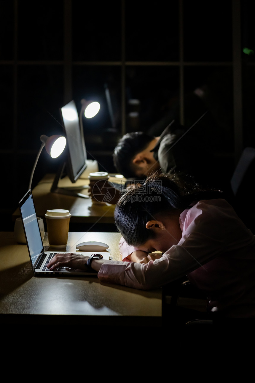 年幼疲劳的女商人深夜睡在办公室的电脑柜台图片