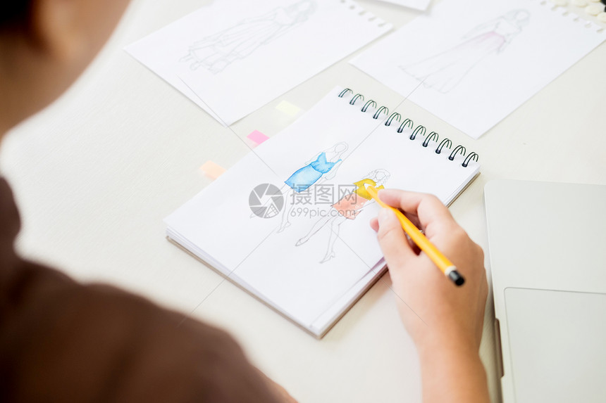 担任时装设计师的年轻妇女在工作场所室画用面纸为服装绘制草图图片
