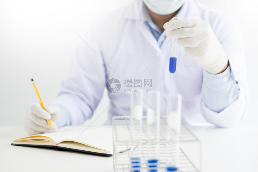 科学家用白色大衣持有和检查试管并用剂记录他在实验室的研究图片