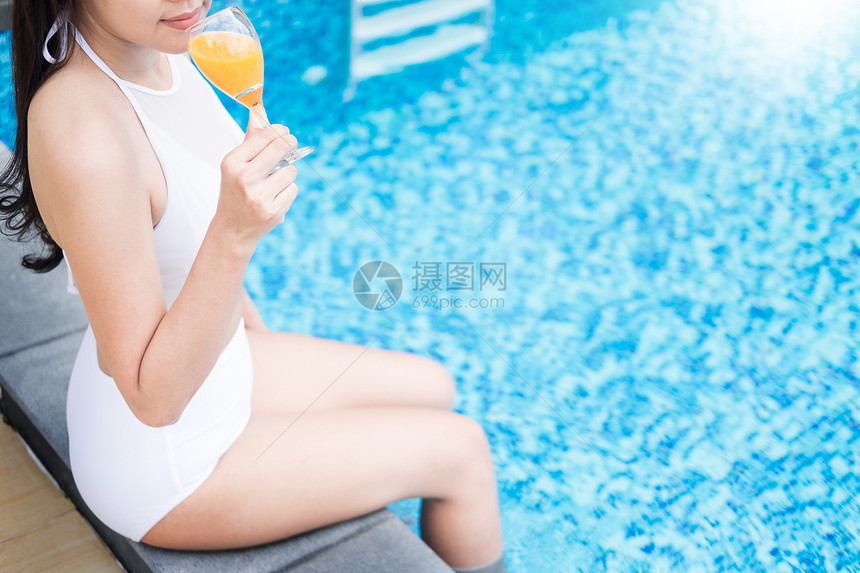 美丽的女孩喝鸡尾酒躺着游泳池暑假概念图片