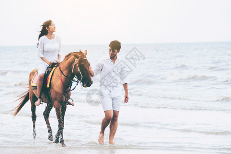 杀马特男生男生牵恋人骑着的马在海边散步背景