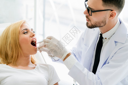 年轻英俊的牙医检查在科诊给女病人检查牙齿图片