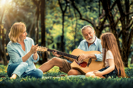 快乐的家庭弹吉他坐在公园里一起唱歌图片