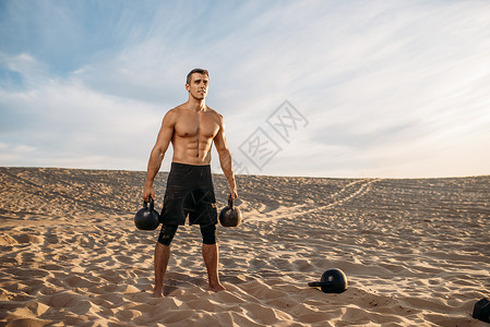 在沙漠用哑铃做运动的男运动员图片