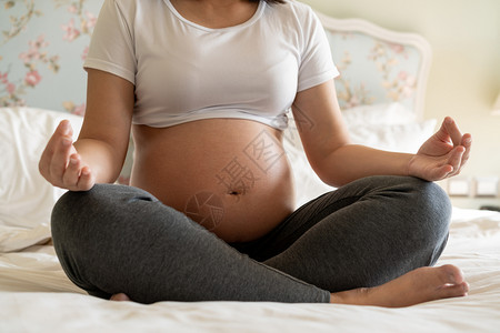 在床上做瑜伽锻炼身体的年轻孕妇图片