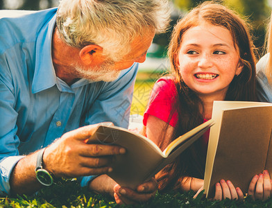 小女孩和父亲在公园草地趴着阅读书籍图片