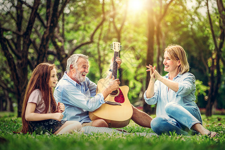 快乐的家庭坐在公园里弹吉他一起唱歌背景图片
