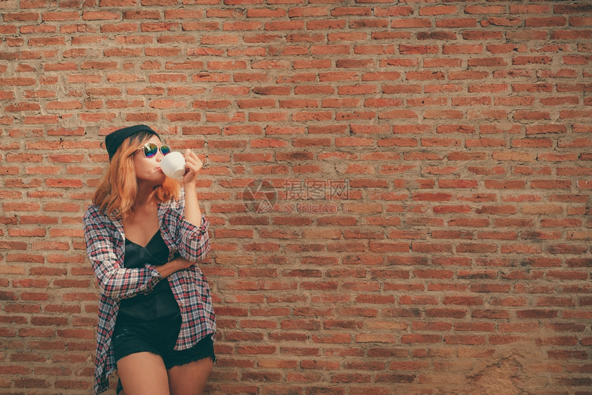 快乐的年轻时髦女人站在街上砖墙旁边手里拿着咖啡杯图片