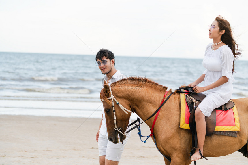 年轻夫妇在热带海滩骑马图片
