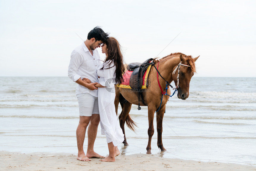 年轻夫妇在热带海滩骑马图片