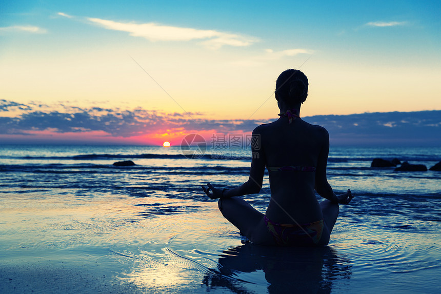 日落时坐在沙滩上冥想的女人图片