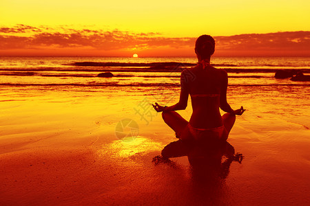 日落时坐在沙滩上冥想的女人图片