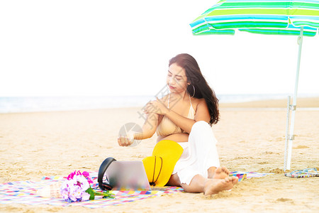 夏天坐在热带沙滩上的年轻女子左手抚摸右手图片