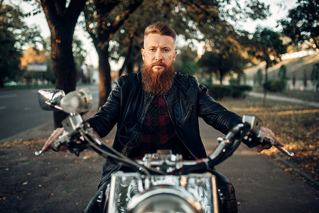 穿着皮夹克的长胡子摩托车手坐在古典直升机前视旧式自行车骑摩托的手背景图片