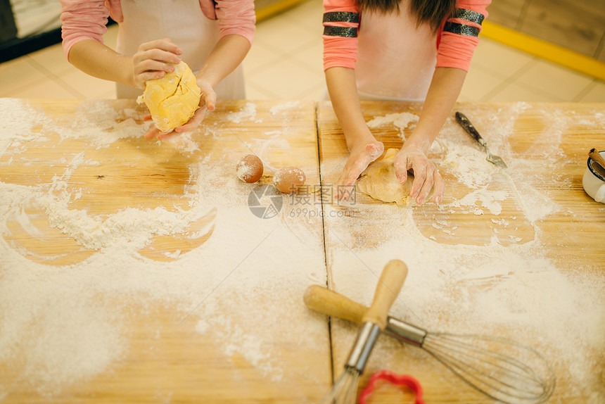 两个小女孩厨师揉面团在厨房准备做饼干图片