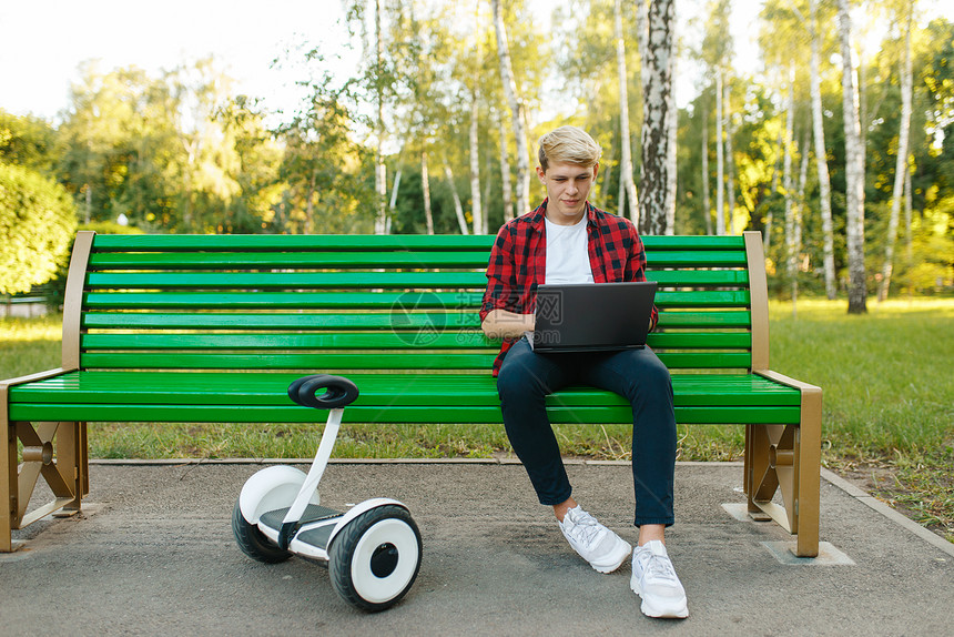 在公园的长椅上坐着带平衡车的年轻男子图片