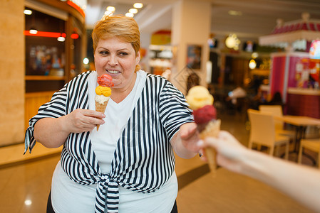 胖女人在快餐商场厅买两块冰淇淋超重女吃冰淇淋肥胖症女人吃冰淇淋快餐店背景图片