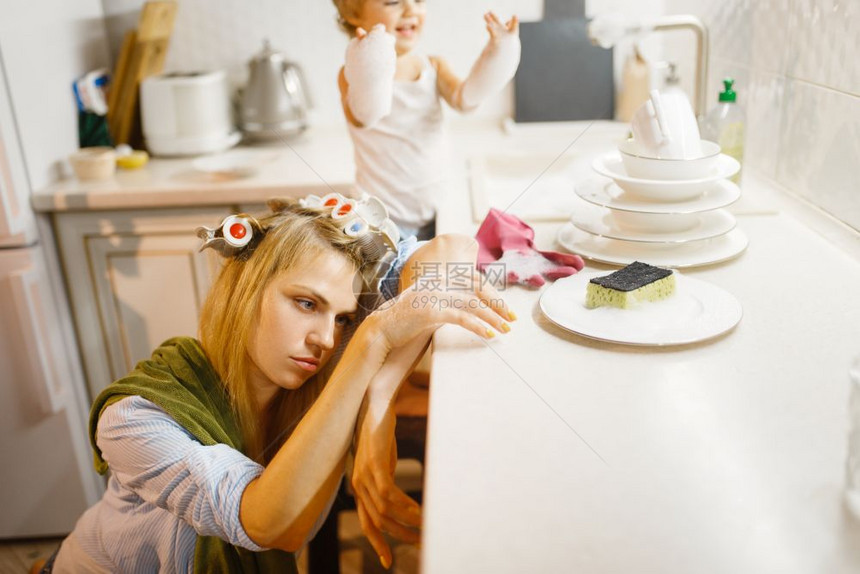 女孩在疲劳的家庭主妇附近洗盘子图片