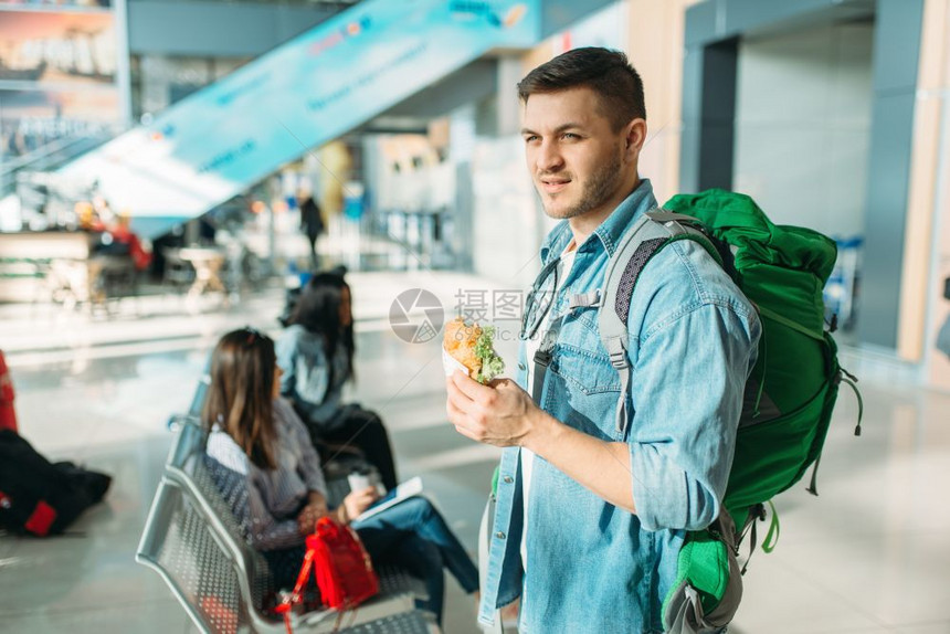 携带背包的男旅游者手拿汉堡在机场等待图片
