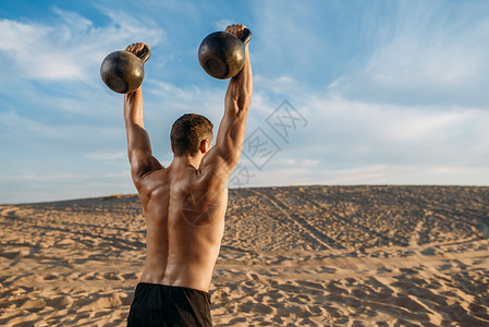 在沙漠上双手分开举着壶铃的肌肉男背部图片