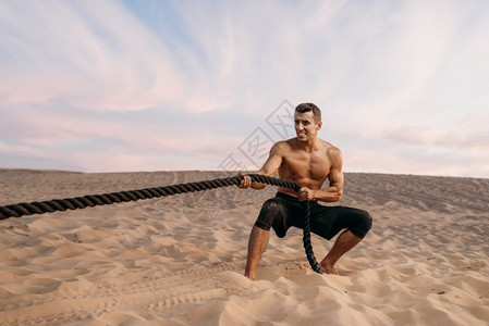 沙漠上男运动员进行拉绳锻炼图片