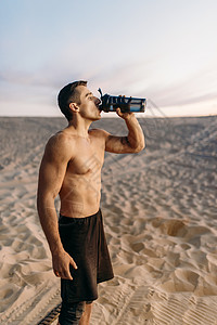 男运动员在阳光明媚的沙漠中喝水图片