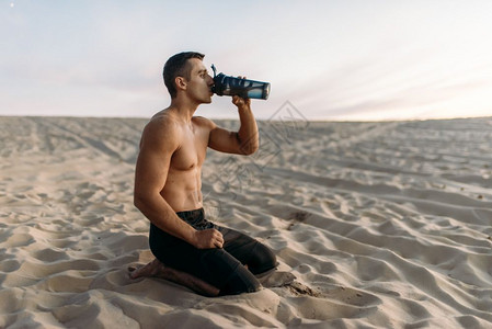 在沙漠中男运动员锻炼后跪坐喝水图片