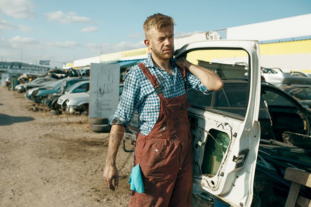 男修理工在汽车垃圾场上将废弃车门回收图片