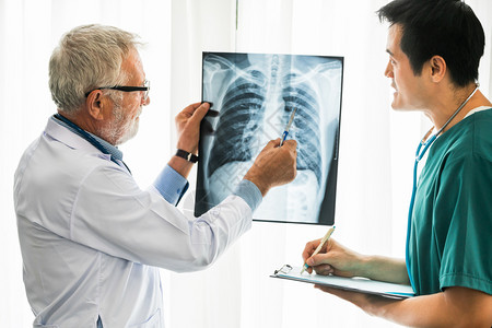 高级男医生在院与另一名生务人员和生一起工作时检查病人胸部受伤的x光片图片