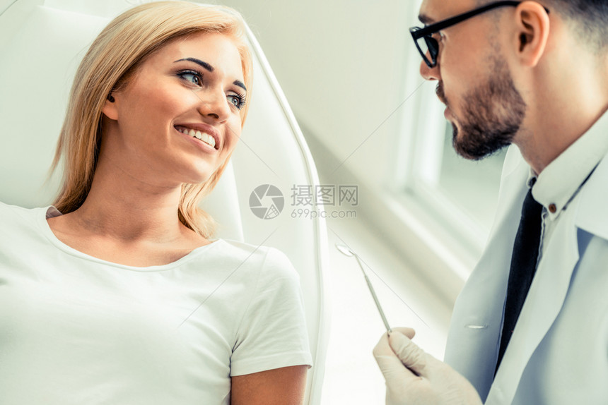 年轻英俊的牙医与坐在椅子上的女病人交谈图片