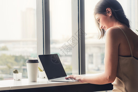 坐在办公室窗户旁边的咖啡厅桌前使用笔记本电脑图片
