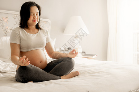 怀孕妇女在家里卧室的床上做瑜伽锻炼图片