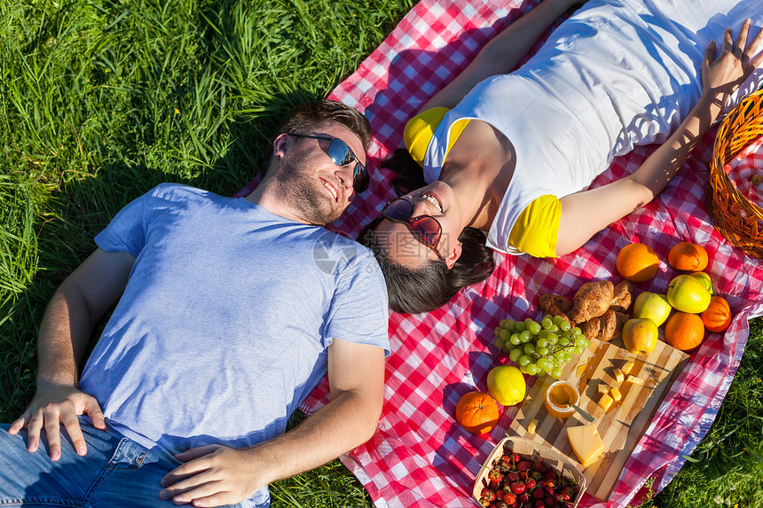 在野餐时躺毯子上的一对年轻夫妇图片