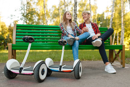 在公园的长凳上坐着旋带板的年轻夫妇用电旋带板进行户外娱乐图片