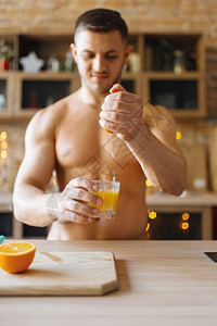 裸体男子在厨房煮橙汁。 裸体男子在家准备早餐,不穿衣服准备食物。图片