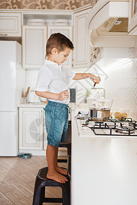 站在碗里男孩站在炉子的椅上准备甜点背景