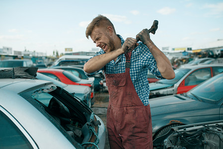 男修理工在汽车垃圾场上用锤子砸车背景图片
