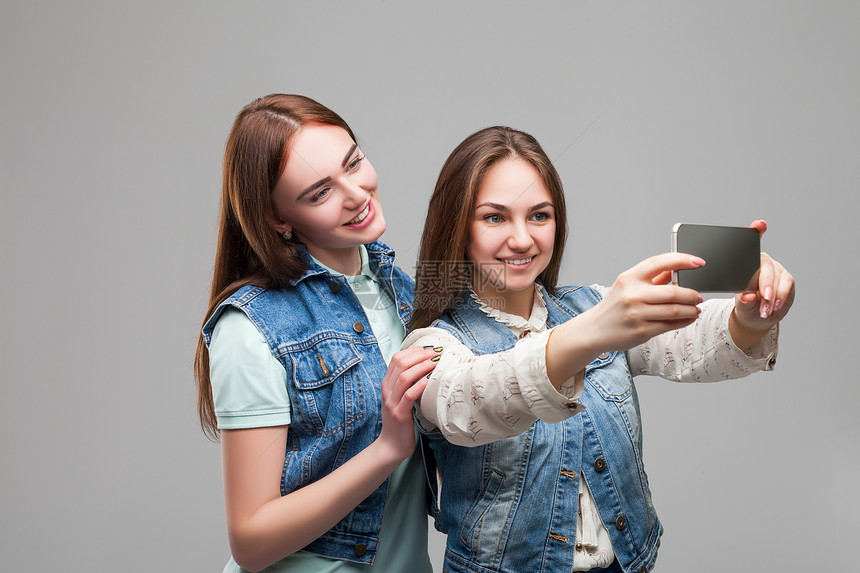 两个女友穿牛仔裤夹克在电话上自拍图片