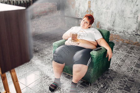 坐在椅子上喝啤酒贪食症肥胖不健康生活方式肥胖女超重妇喝啤酒背景图片