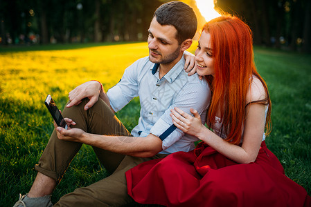 情侣坐在公园草地上玩手机图片